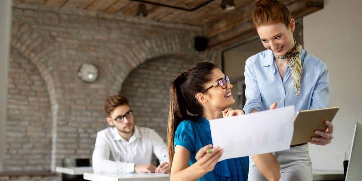 Student zeigt Lehrer ein Blatt, ein anderer sitzt dahinter.