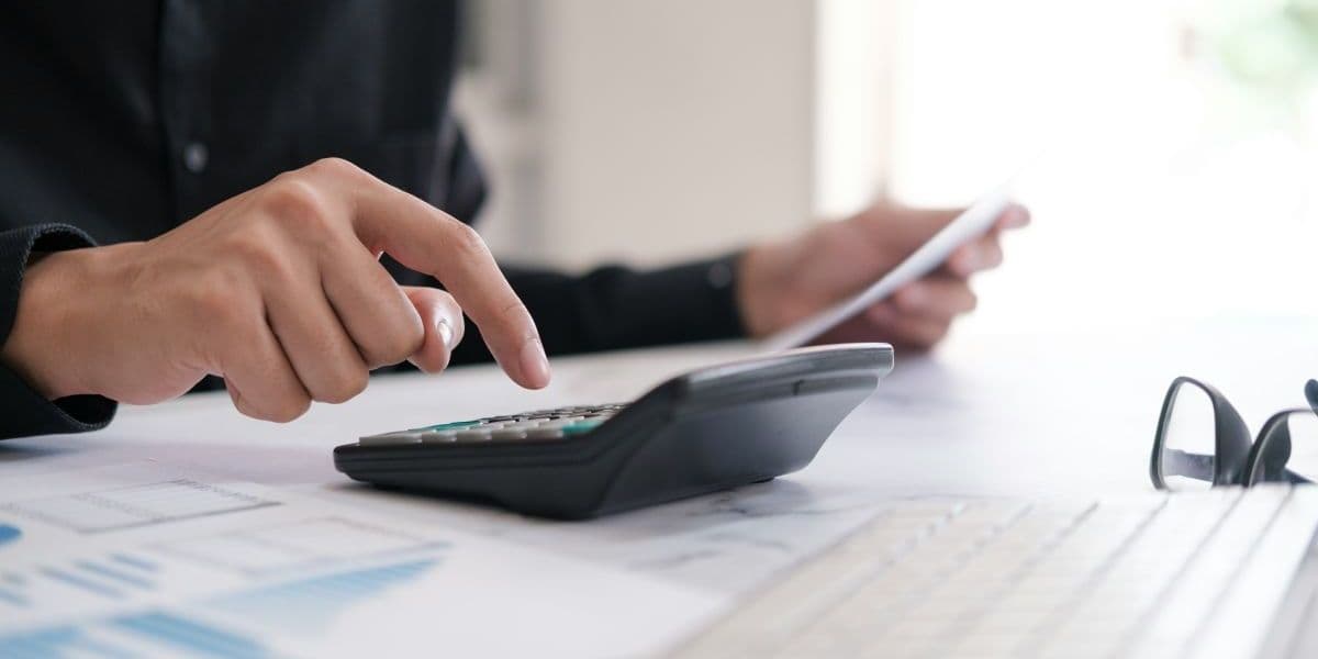 Büromitarbeiter nutzt Taschenrechner und Laptop zur Planung von Budget und Karrierefinanzen.